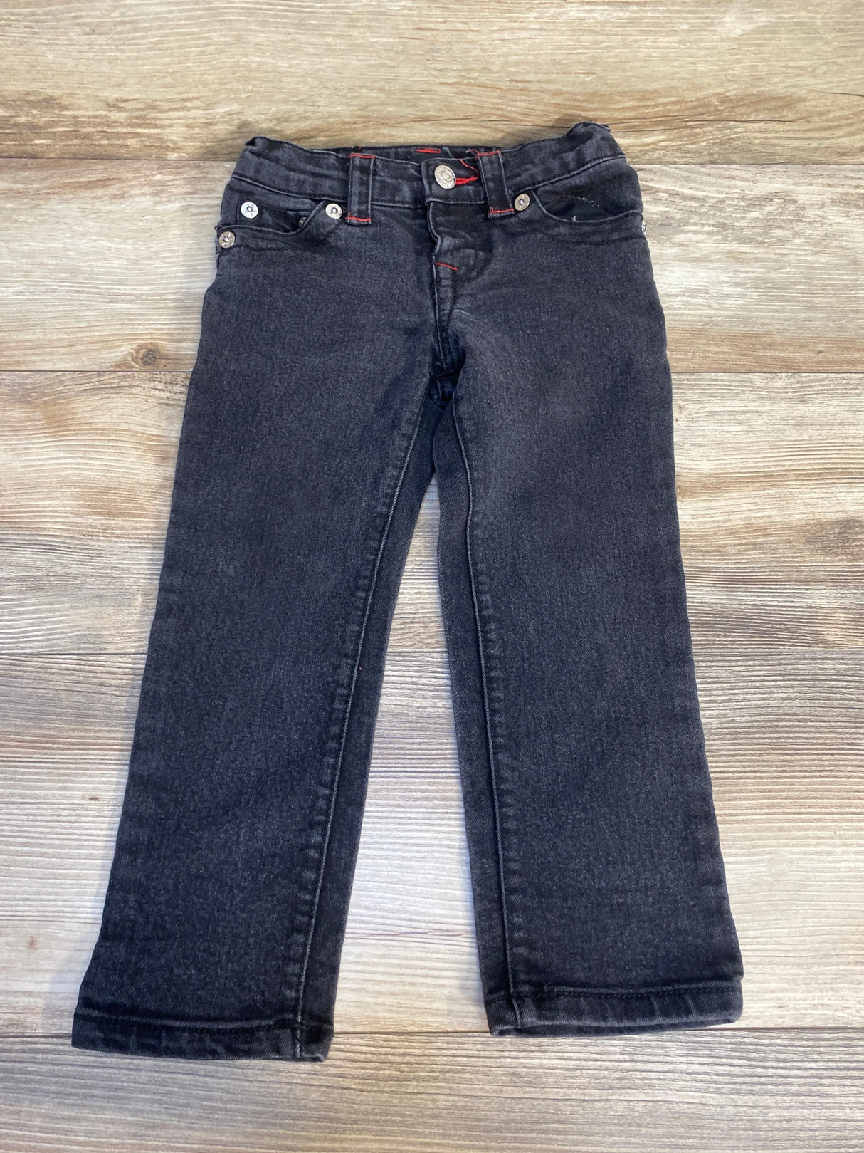 Black kids' jeans with red stitching on wood background, gently used children's clothing