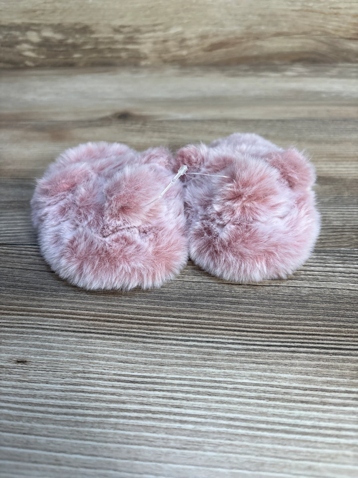 Soft pink faux fur baby booties on wood background, kids footwear resale.