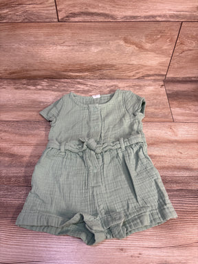 Top-down flat lay of light green Baby Gap muslin shortie romper with front snaps and tied waist belt on wood background