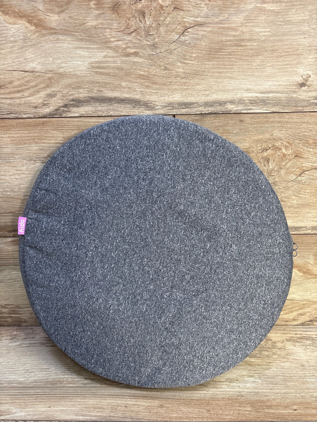 Top-down view of Frida Mom donut pillow showing heather-gray fabric cover and pink Frida tag on wood background