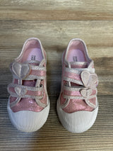 Pink glitter toddler shoes with heart-shaped straps on wood background