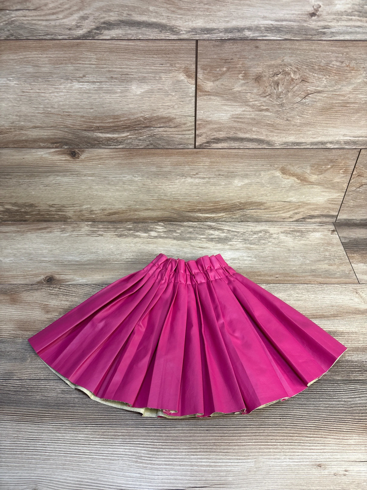 Bright pink pleated kids skirt on wood floor, perfect for children's fashion and resale clothing