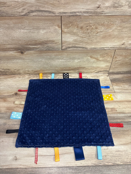 Top view of blue minky dot tag ribbon baby blanket showcasing colorful ribbons around the edges on a wood background