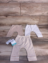Flat lay of three newborn Disney Baby pants, tan dotted, light gray, and tan-and-white striped, showing elastic waists on wood background