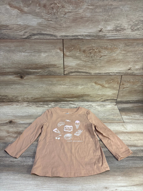 Front view of Cat and Jack tan snack shirt in size 2T showcasing food graphics and long sleeves on a wood-grain background