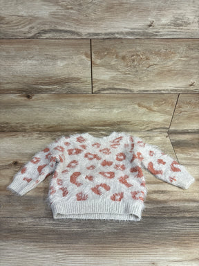 White fuzzy toddler sweater with orange leopard print pattern on wooden floor