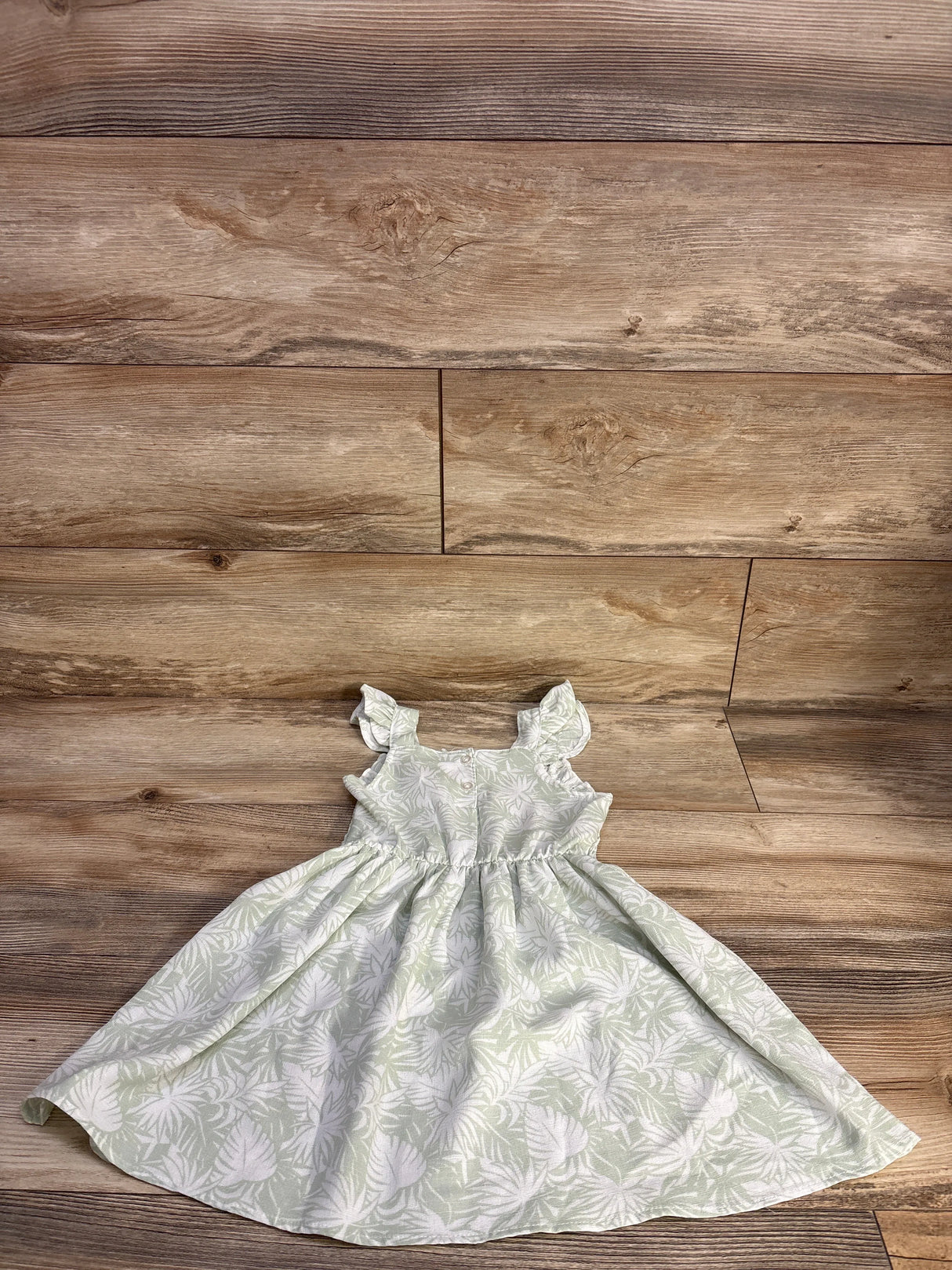 Flat lay of Little Lass smocked girls' dress in pale green with white leaf print, ruffle sleeves, gathered skirt, 4T