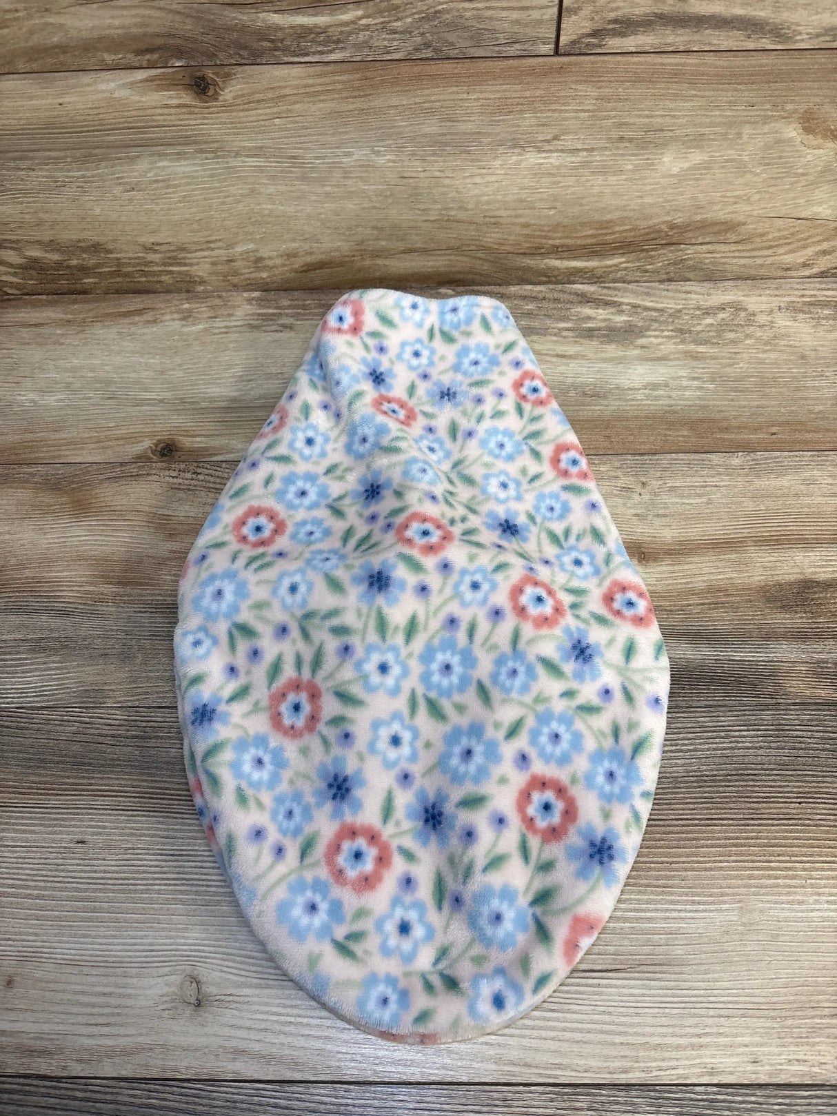 Floral fleece baby hat with blue and pink flowers on light background, laid on wood floor