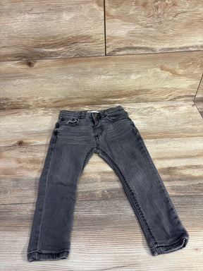 Child-sized black denim jeans laid flat on a rustic wooden floor background