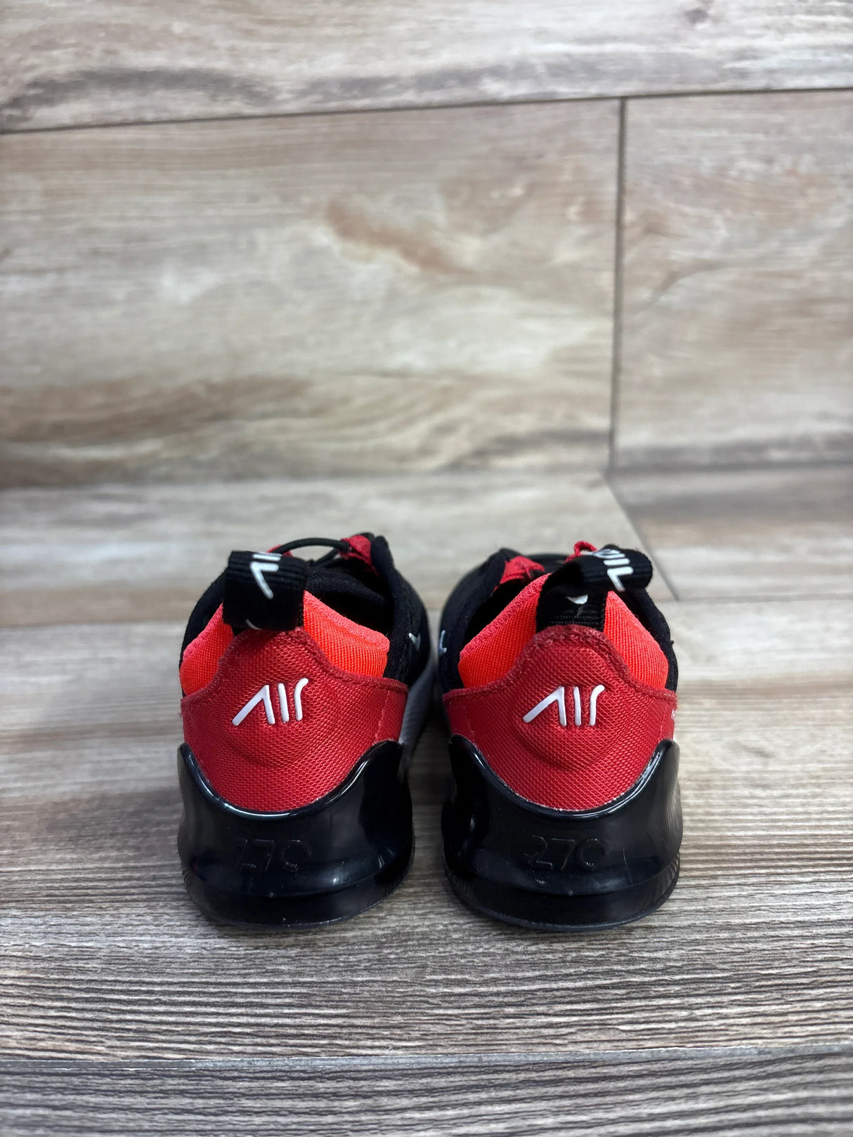 Rear view of Nike Air Max 270 toddler sneakers in black and red showing white AIR heel logo on wood floor