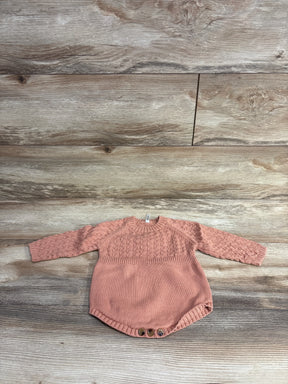 Pink knitted baby onesie with long sleeves and buttons on wooden floor