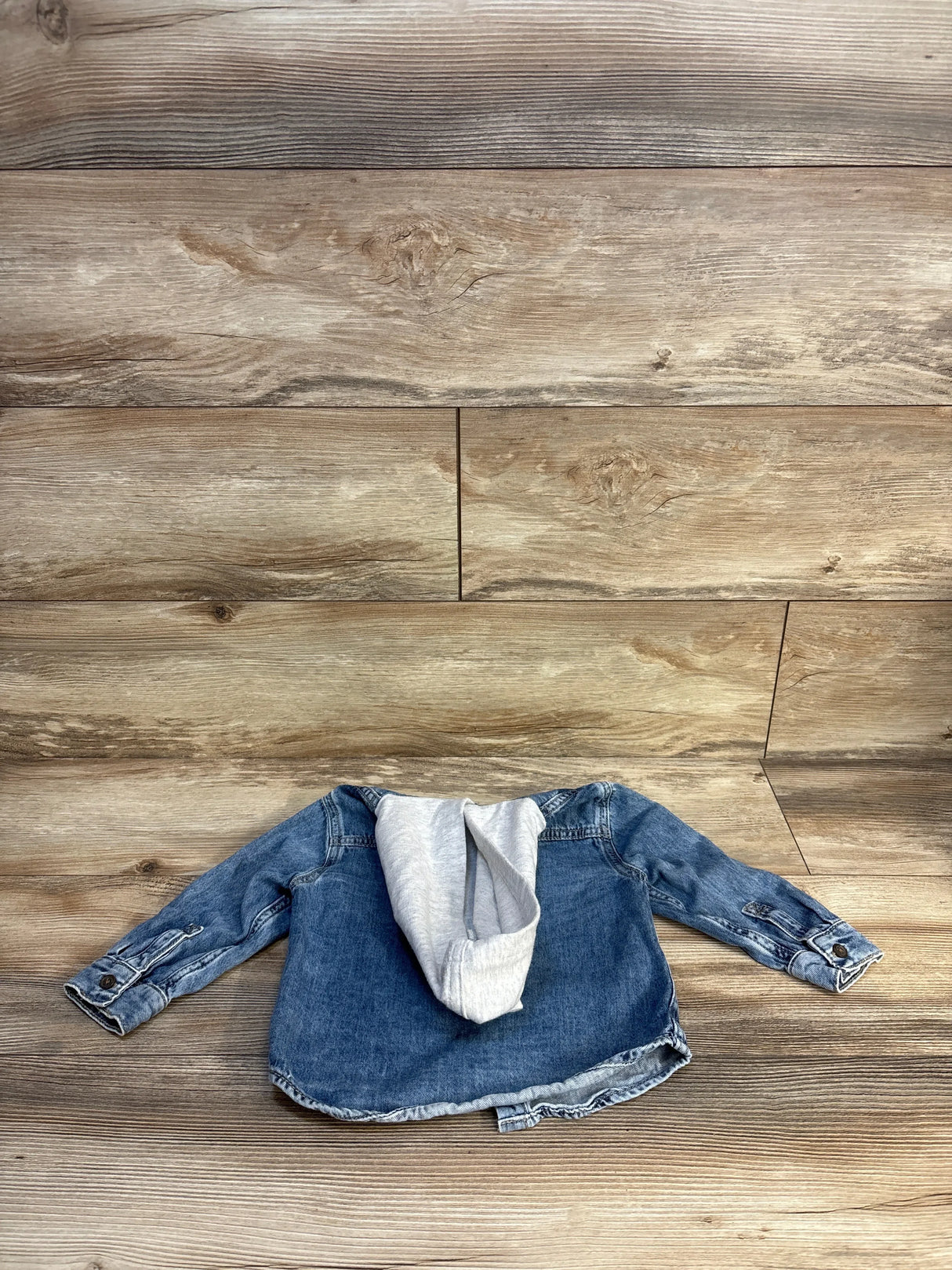 Kids denim jacket with gray hoodie lining, laid flat on wood floor