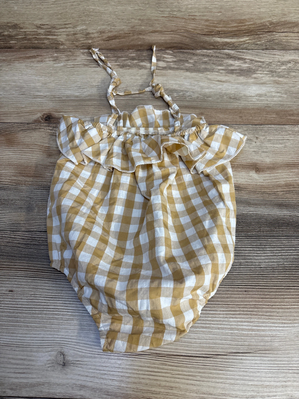 Yellow and white gingham baby romper with ruffled straps and elastic waist, laid on wood floor