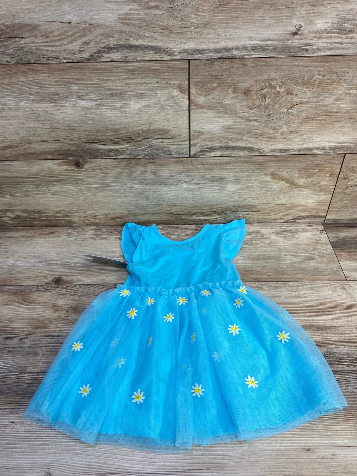 Flat lay of turquoise toddler tulle dress size 2T with daisy appliqués, flutter sleeves, full skirt on wood background