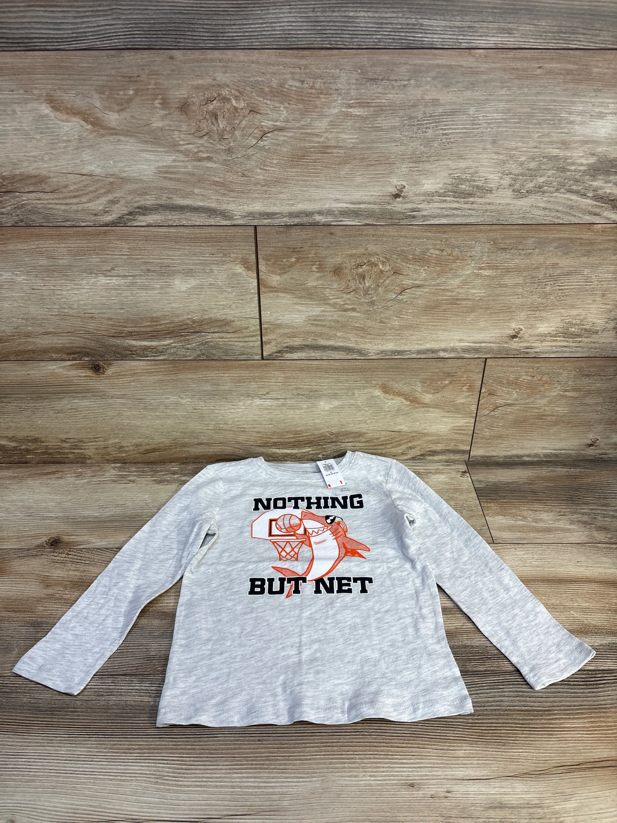 Gray kids long sleeve shirt with 'Nothing But Net' shark graphic, laid on wood floor