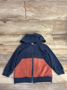 Kids zip-up hoodie with navy blue top, rust orange pockets and hood, laid on wood floor