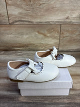 Side view of white leather baby Mary Jane flats size 7C showcasing scalloped trim and bow on white box, wood floor background