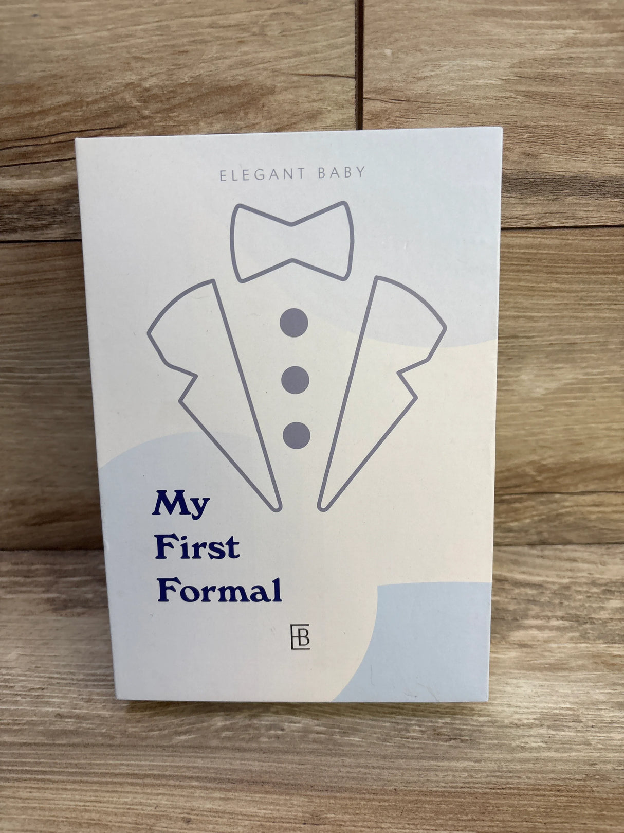 Front of Elegant Baby onesie box labeled My First Formal showing printed tuxedo graphic on wooden surface