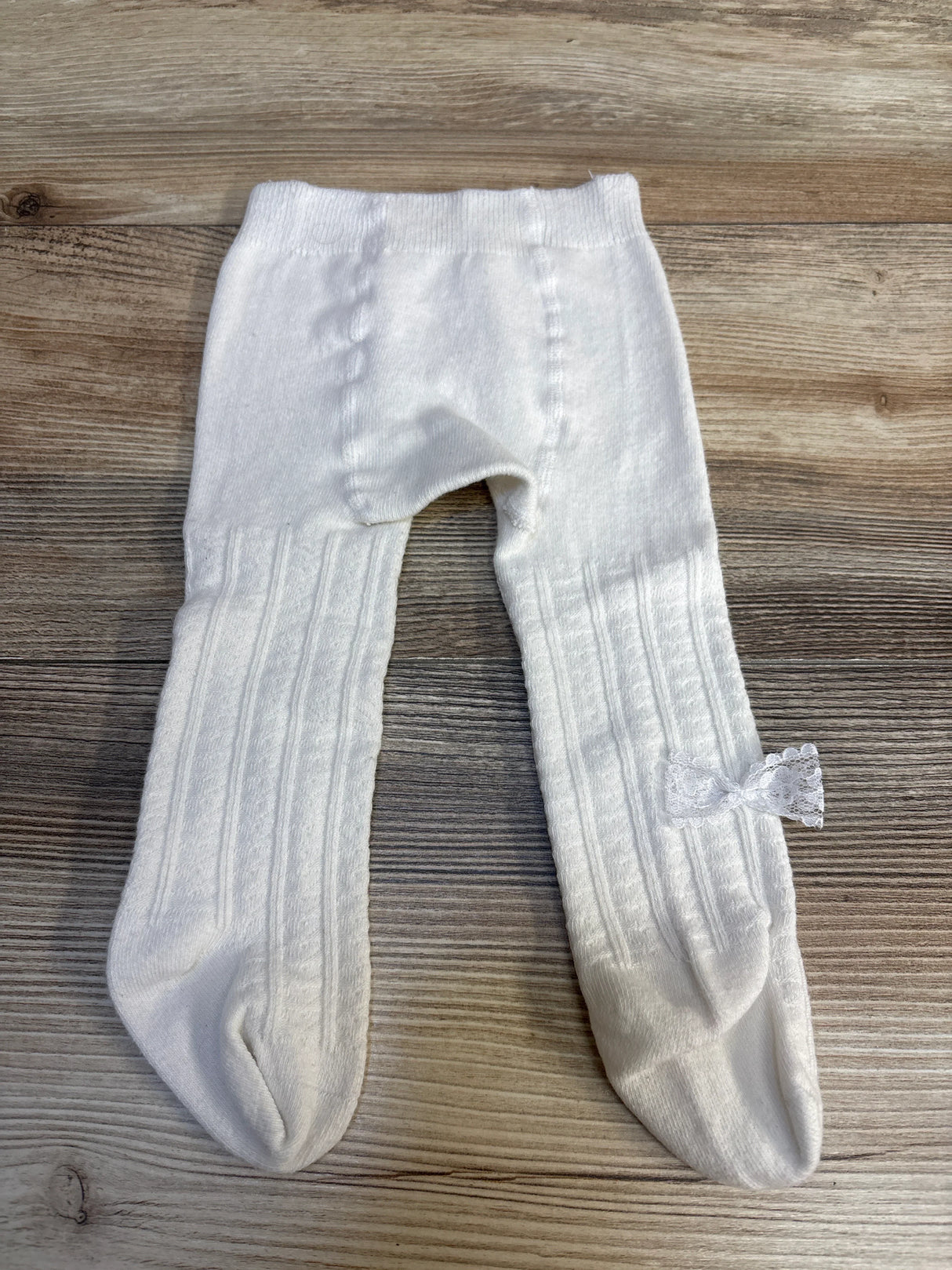 White baby tights with lace bow, ribbed texture, laid on wood floor — kids clothing resale