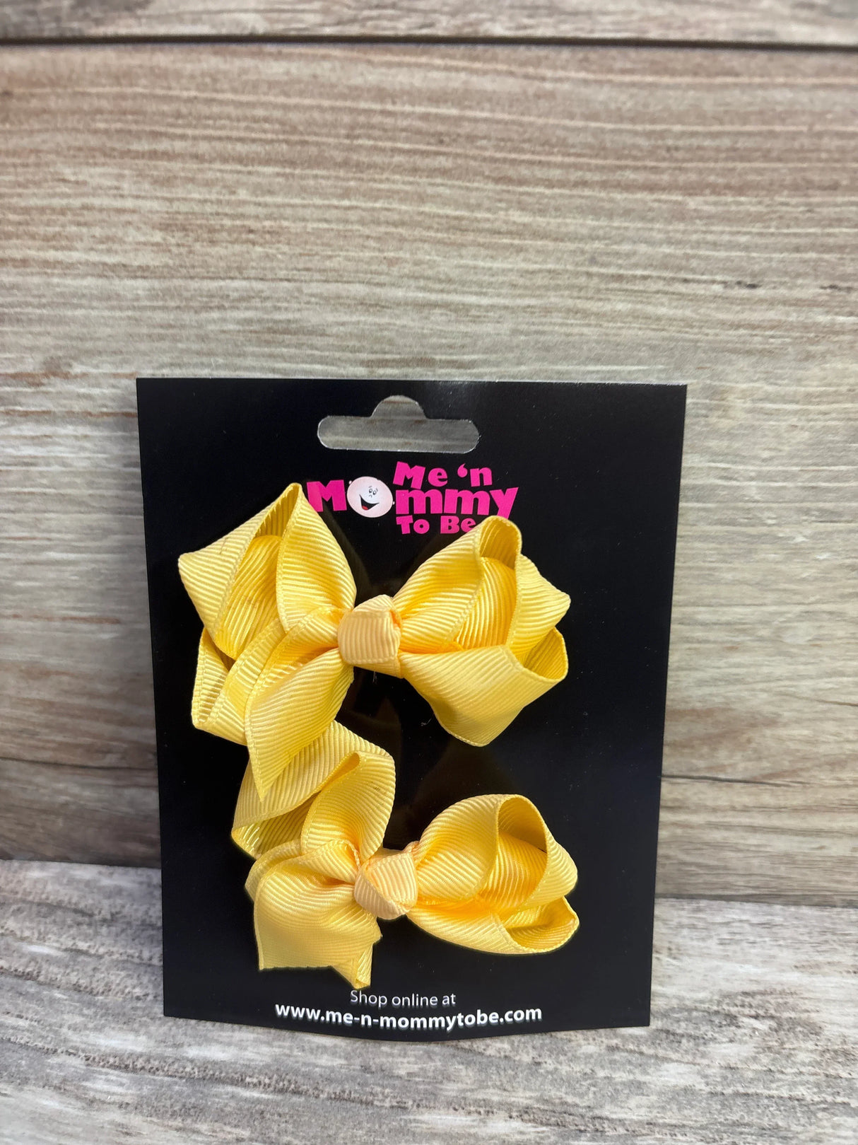 Front view of two yellow grosgrain ribbon hair bows showcasing bow loops and knot on a black branded display card with wooden plank background