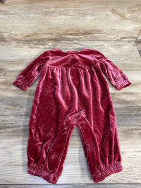 Red velvet long-sleeve baby romper with gathered cuffs and small bow, laid on wooden floor