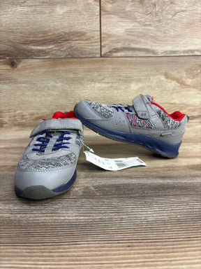 Pair of gray and blue children's sneakers with red lining and Velcro straps on wooden surface