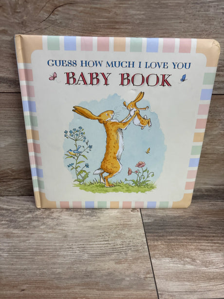 Front view of Guess How Much I Love You hardcover baby book showcasing adult and baby rabbits with a pastel border on a wood tabletop