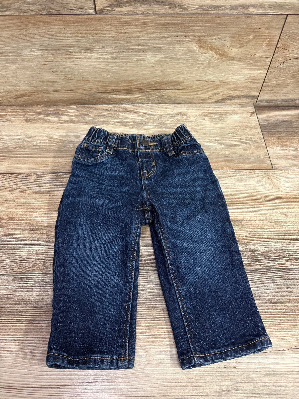 Dark wash navy blue baby jeans for size 6-12m laid flat on a wooden surface.