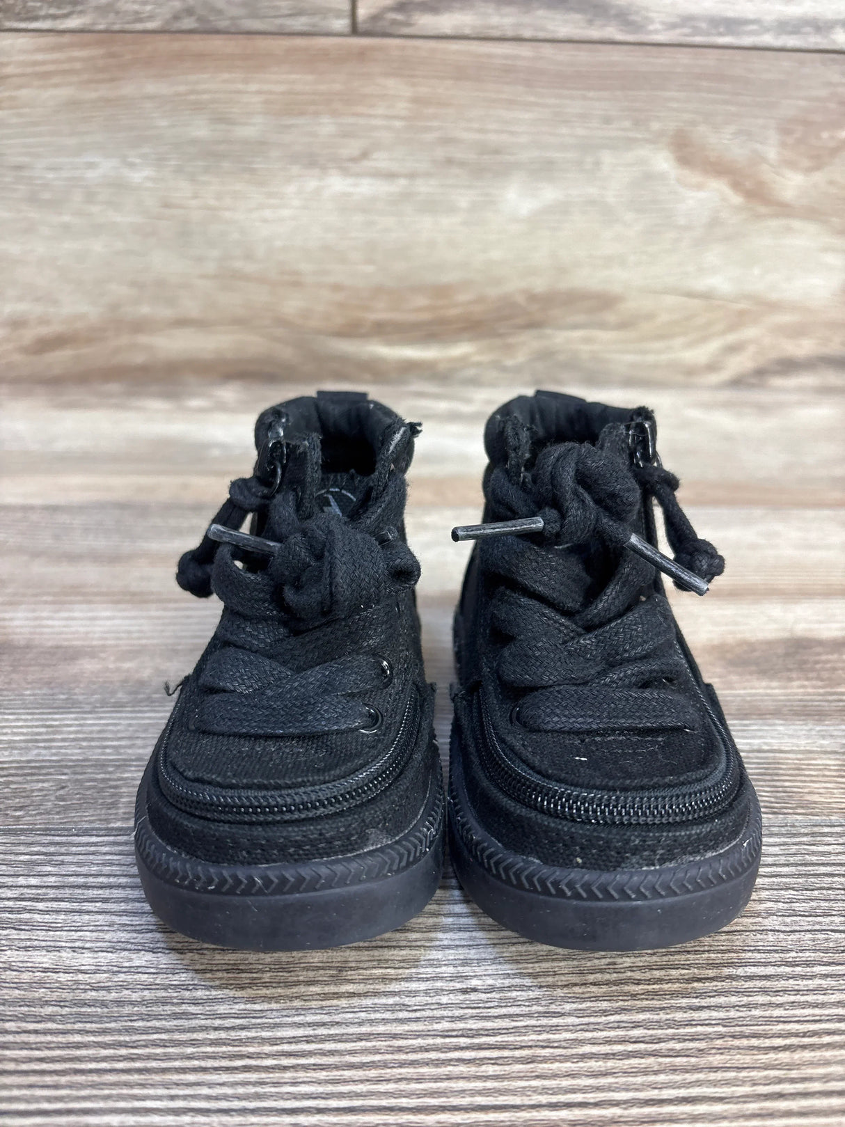 Front view of Billy Footwear adaptive black high-top toddler sneakers with laces, side zippers and rubber sole on wood