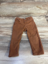Front flat-lay of brown H&M twill baby pants (12m) showing elastic waist, front pockets, tapered legs on wood background