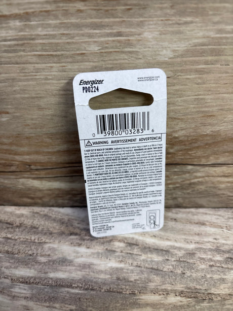 Back view of Energizer 2025 lithium coin battery 2-pack showing barcode and warning text on cardboard backing with wood background