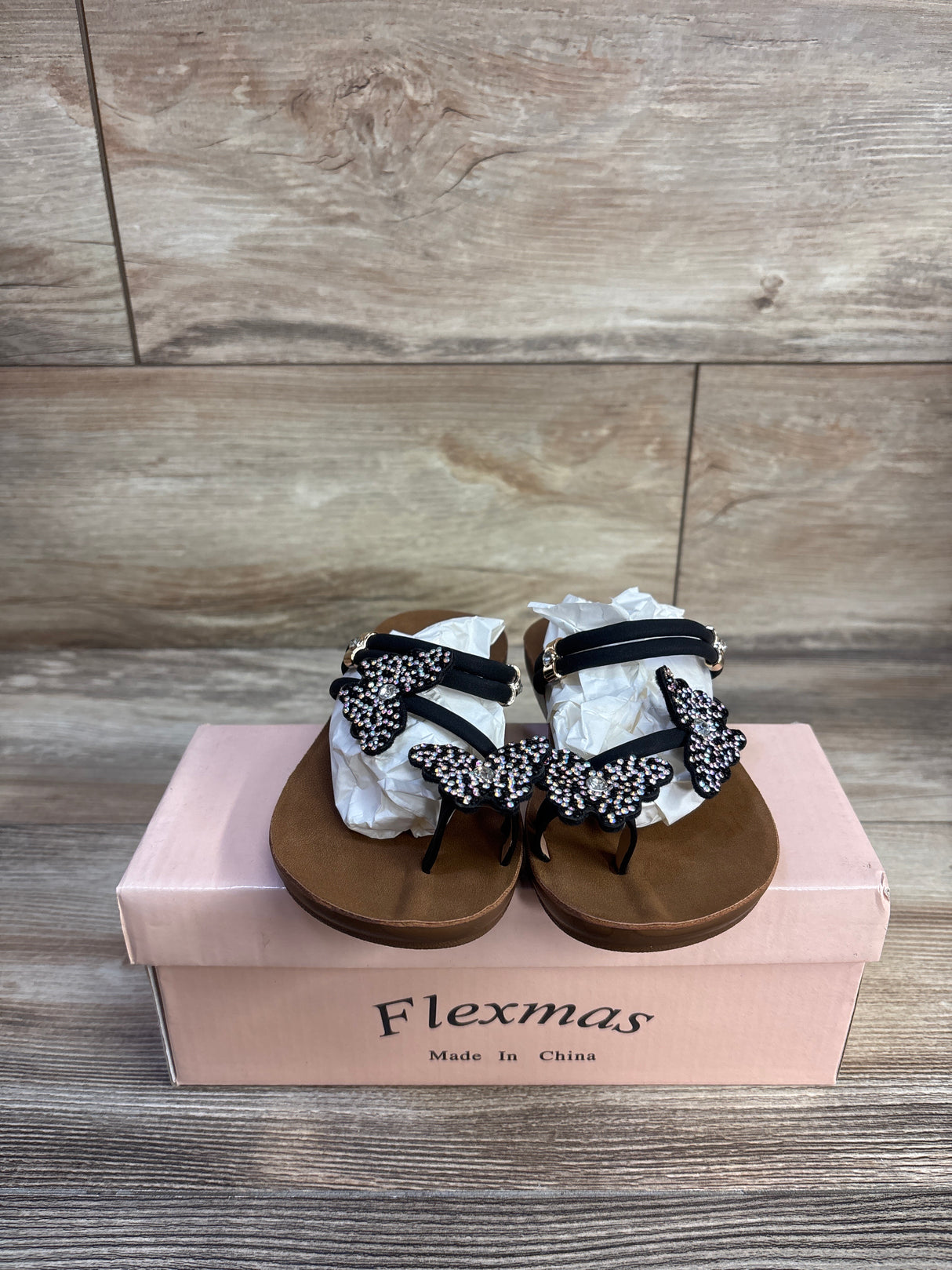 Front view of Flexmas toddler sandal, size 10C, brown footbed with black straps and rhinestone butterfly decorations on pink box