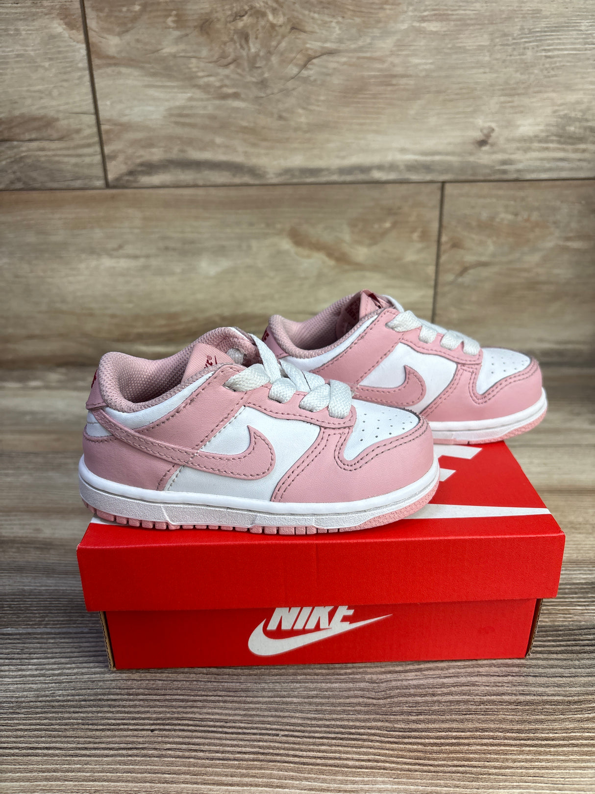 Side view of toddler Nike Dunk Low 'Pink Glaze' sneakers, size 8C; pink and white leather with white laces on a red Nike box