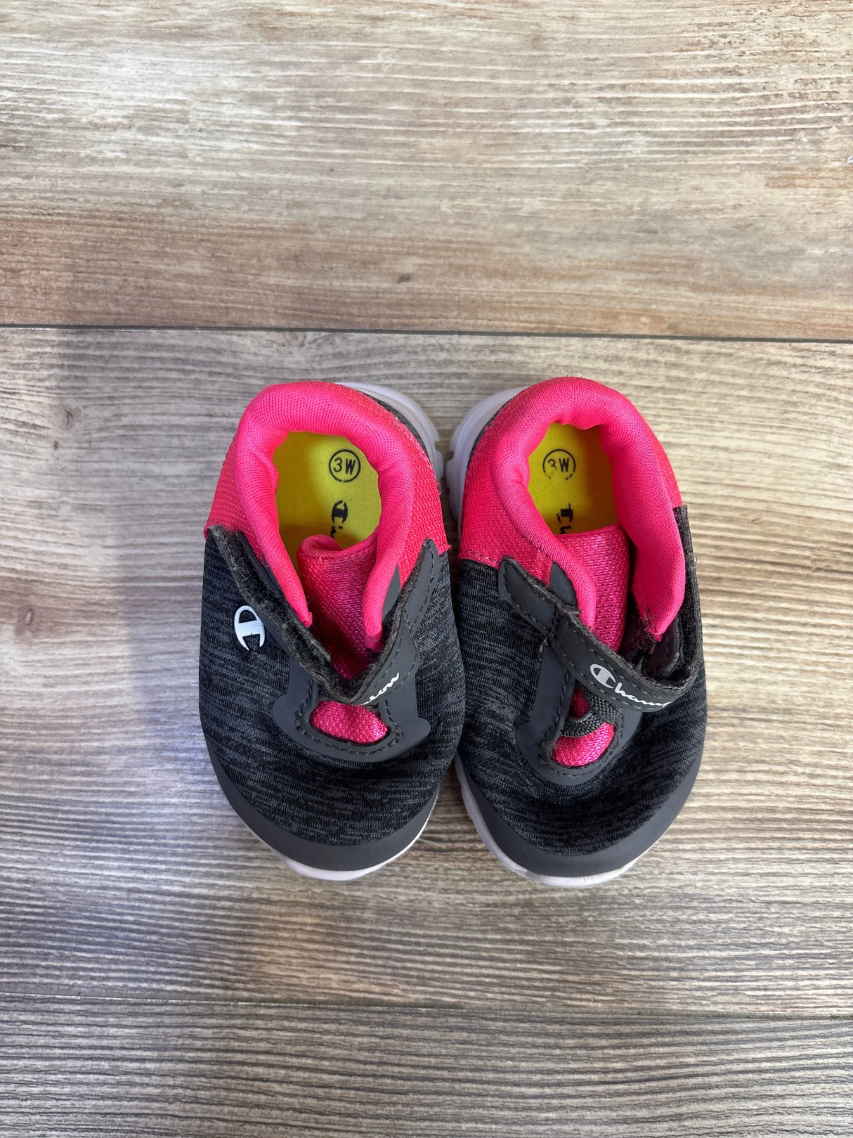 Top view of Champion toddler sneakers, gray knit with pink lining and velcro strap, size 3W on yellow insoles on wood floor