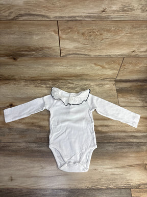 White long-sleeve baby bodysuit with a ruffled collar and black trim on wooden floor
