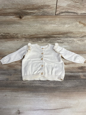 Cream-colored toddler cardigan with wooden buttons and ruffle details on sleeves on wooden floor