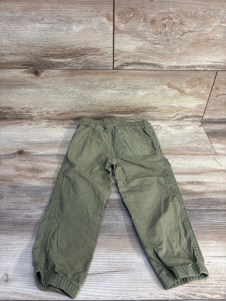 Flat lay back view of toddler green drawstring pants showing elastic waist, patch pocket and elastic cuffs on wood floor