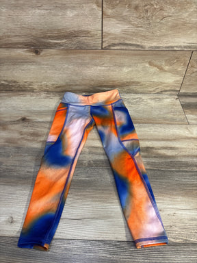 Front flat-lay of girl's orange and blue leggings with high waistband, side pockets and contrast flatlock seams on wood floor