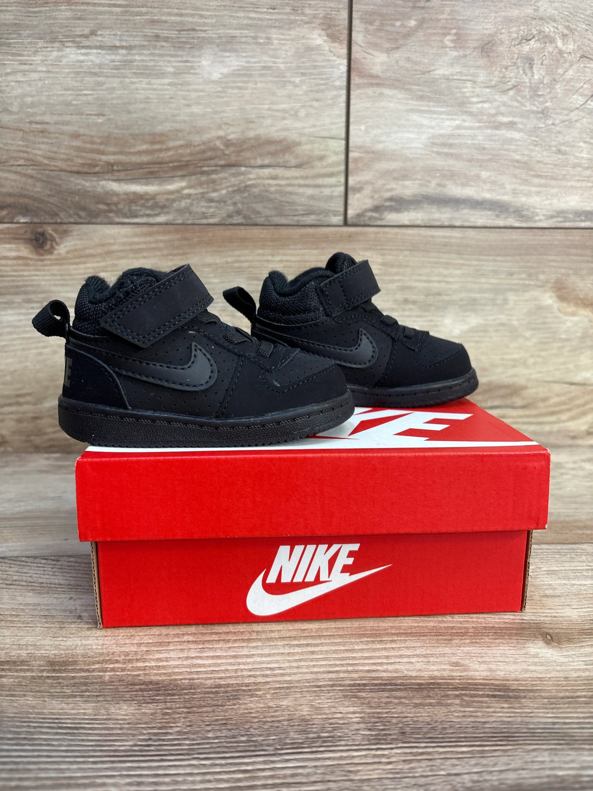 Black Nike toddler sneakers with velcro straps on red shoebox