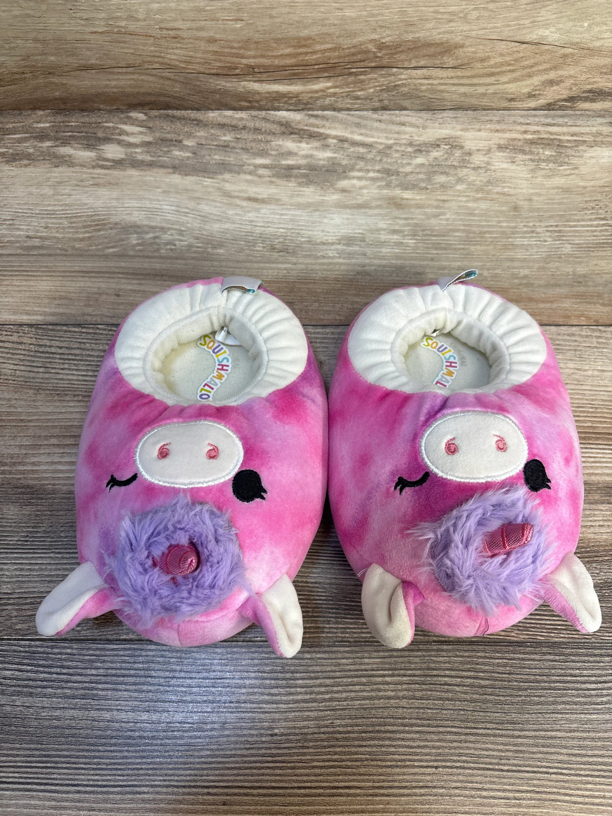 Pink pig plush kids slippers with purple snout on wood floor, gently used.