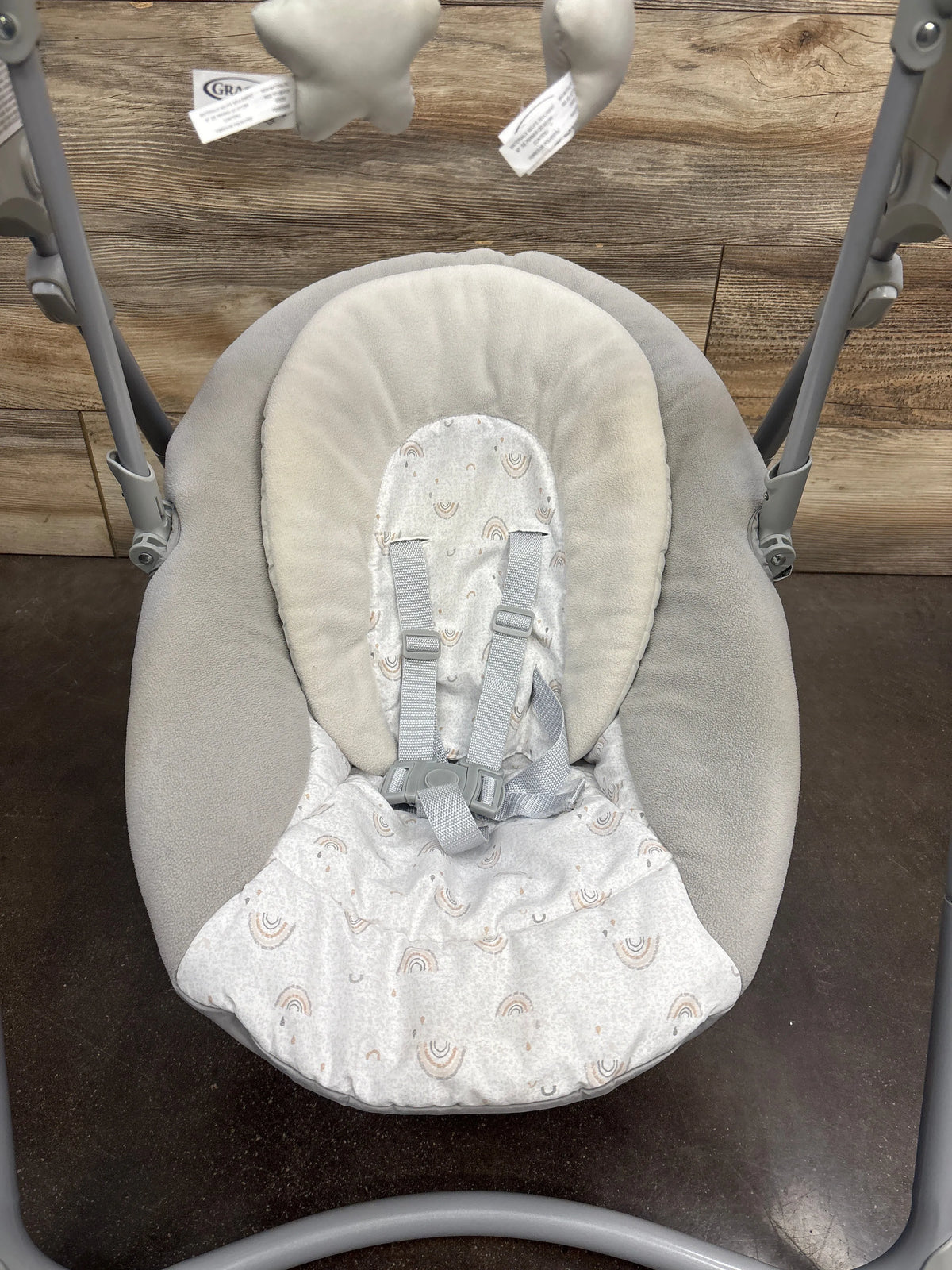 Front view of Graco Slim Spaces Compact Baby Swing in Reign with rainbow-patterned padded seat and harness