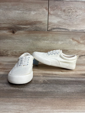 White canvas kids sneakers with laces on wooden floor, gently used children's shoes