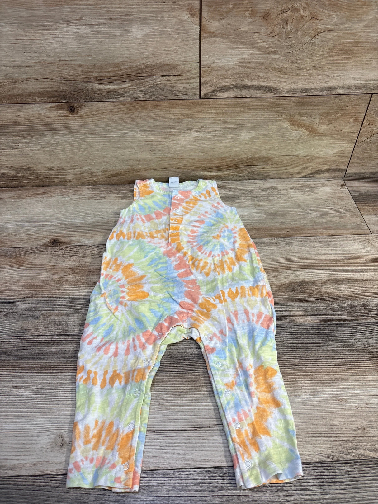 Flat-lay of toddler tank romper (18-24 months) showing front snap closures and pastel tie-dye on wood background