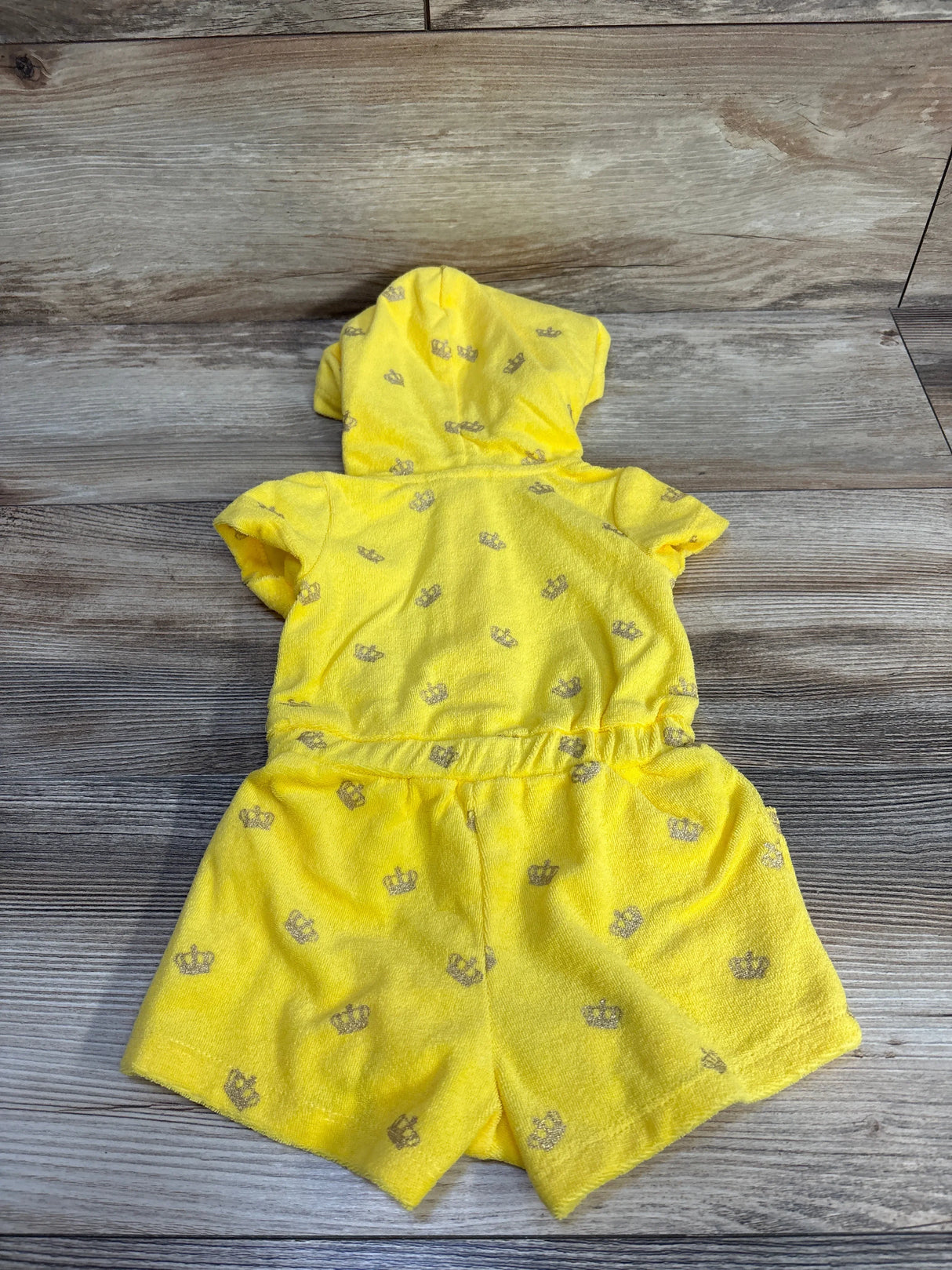 Back flat-lay of yellow Juicy Couture terry shortie romper with hood, short sleeves, elastic waist, and silver crown print