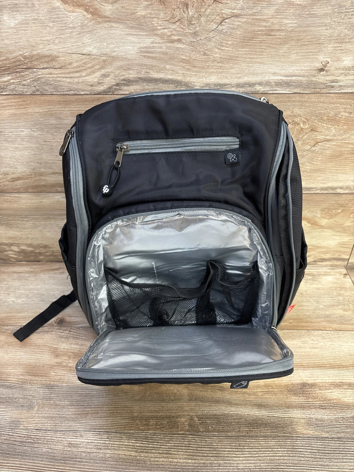 Front view of Fisher Price Kaden FastFinder diaper bag backpack showing open insulated front compartment with mesh pockets on wood floor background