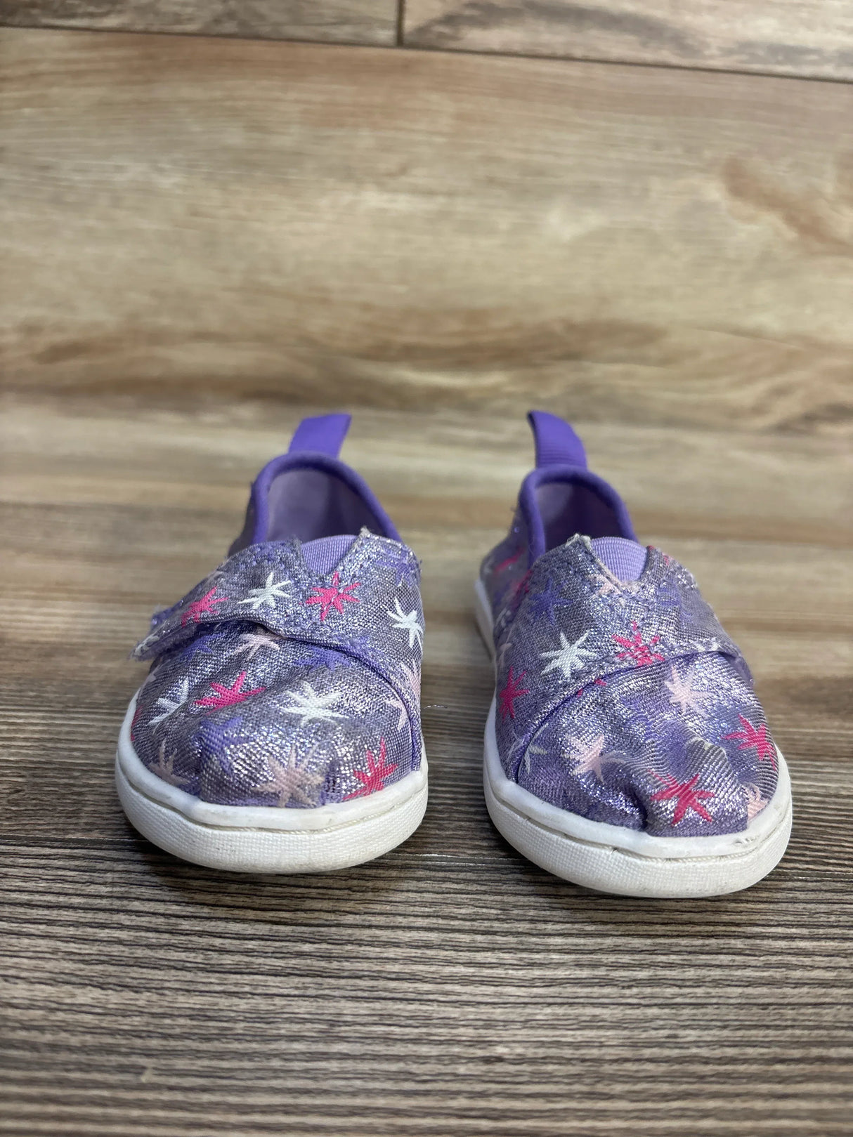Purple kids' slip-on sneakers with starfish print, glitter fabric, and white soles on wood floor