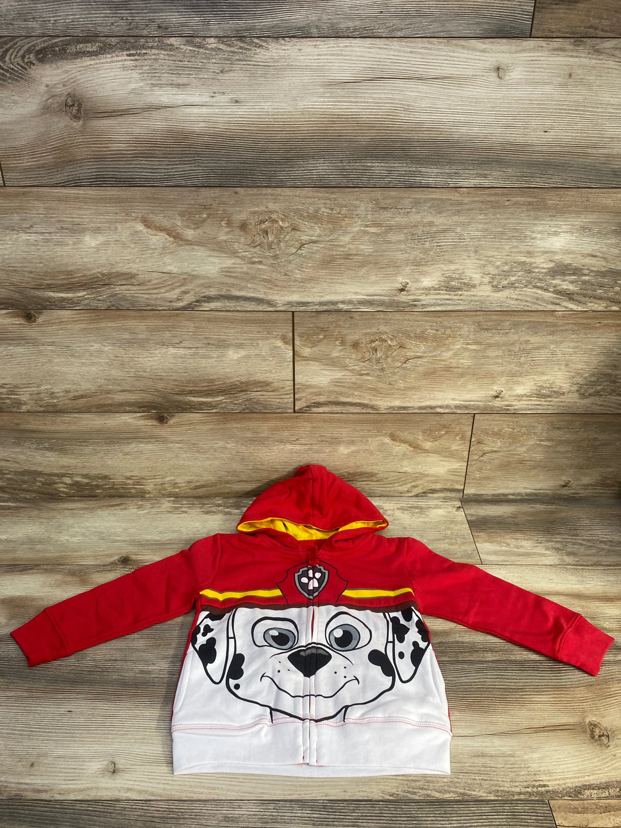 Flat lay of red toddler Paw Patrol Marshall zip-up hoodie size 4T showing large front face print and yellow-lined hood on wood floor