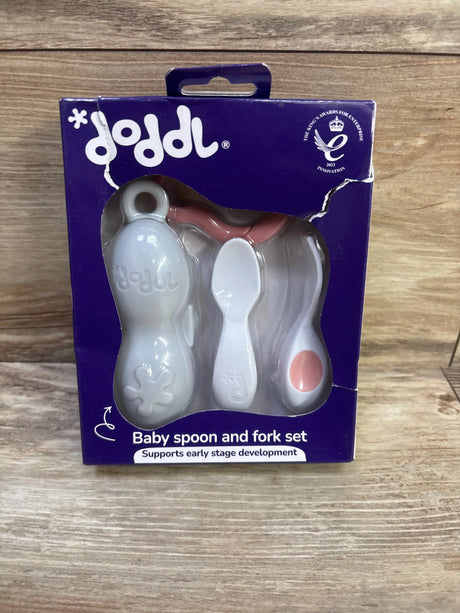 Front view of Doddl baby spoon and fork set in purple packaging with white utensils and pink accents on a wood surface