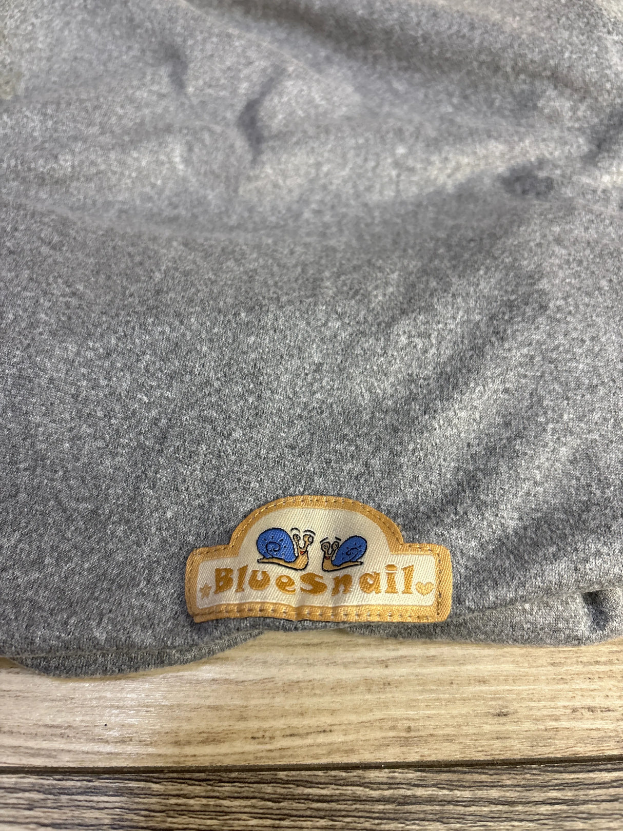 Close-up of BlueSnail soft stretchy bassinet sheet showcasing embroidered Bluesnail label with two blue snails on a wooden surface