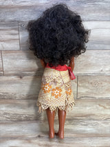 Rear view of 32-inch Moana doll showing curly dark hair, patterned skirt and red sash against wood plank background